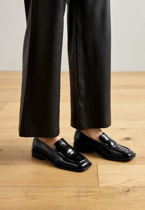 Fekete lakkbőr loaferek sima, fényes felülettel, alacsony blokk sarkú és klasszikus, ívelt vonalakkal rendelkező dizájnnal.