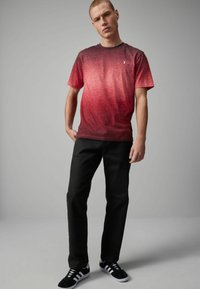 Camiseta de manga corta en degradado rojo con cuello redondo, combinada con pantalones negros y zapatillas negras con rayas blancas.