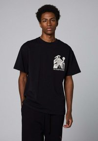 Camiseta de algodón negra con un diseño gráfico en blanco en el área del pecho izquierdo. Mangas cortas y un corte relajado, textura mínima.