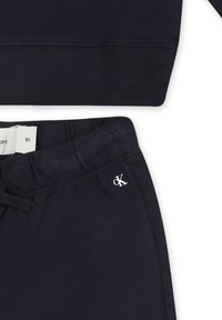 Conjunto de sudadera y pantalones de algodón de color azul marino. Presenta cintura elástica, cordón ajustable y un logo blanco en la prenda. Textura suave.
