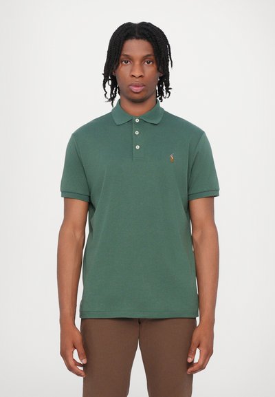 Polo de color verde oscuro con cuello, tres botones, mangas cortas y un pequeño logotipo bordado en el pecho. Textura suave.