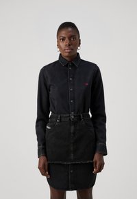 Zwarte denim blouse met knoopsluiting, lange mouwen en een klein rood logo. Gecombineerd met een zwarte denim rok met een rafelige zoom.