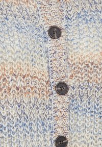 Stickad cardigan i kräm, ljusblå och mjuka orange toner. Har texturerad sömnad och mörka knappar. Närbild av tyg och knappar.