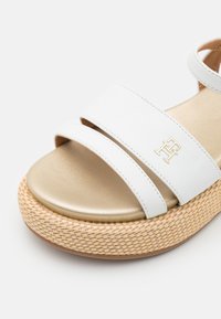 White platform sandals with two wide straps, gold-tone footbed, and woven texture on the natural-colored sole, featuring a small logo.