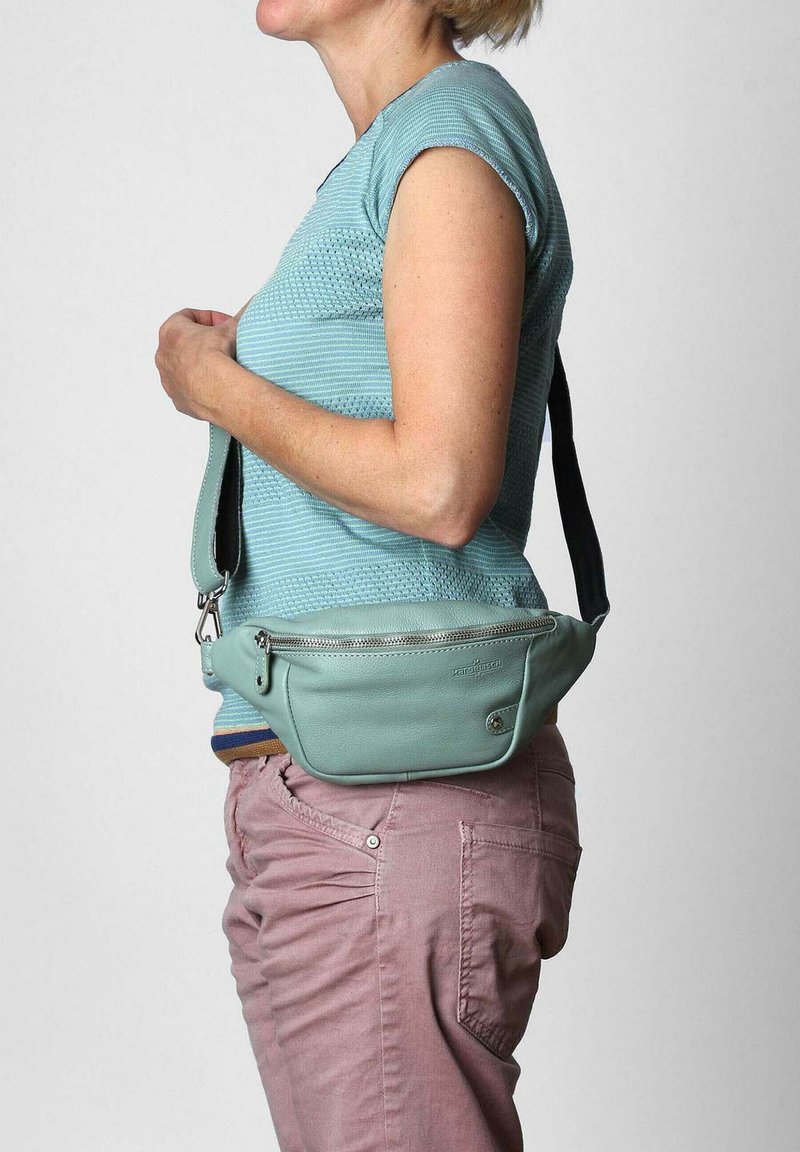 Hellgrüne Leder-Crossbody-Tasche mit einem Reißverschlussfach, verfügt über ein flaches Design und einen verstellbaren Riemen, der um die Taille getragen wird.