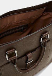 Brun läderväska med textur och rymligt inre, som har en ficka med dragkedja och silverfärgade detaljer. Dubbla handtag för bärande.