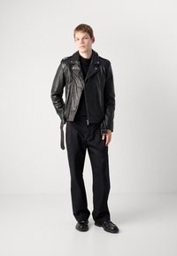 Black leather biker jacket with asymmetrical zipper, shoulder epaulettes, and tailored fit, paired with loose black trousers and black shoes.
