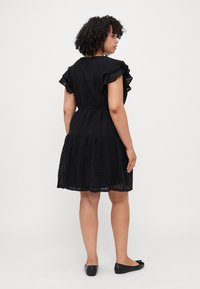 Black lace dress with ruffled short sleeves, fitted waist, and flared skirt. Detailed pattern throughout and worn with black flats.