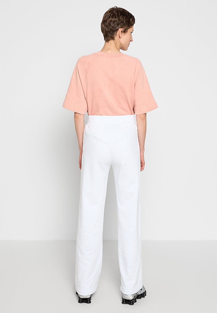 Różowa bawełniana koszulka z szerokimi rękawami w połączeniu z luźnymi, białymi spodniami. Zauważalne detale to elastyczny pas i obuwie z czarnymi akcentami.