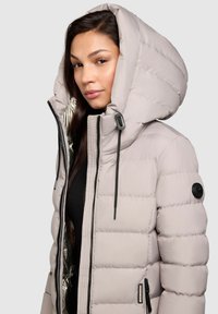 Gai pelēks pūkains apmetnis ar lielu kapuci, ar rāvējslēdzēju priekšā un spīdīgu sudraba oderi. Iekļauj melnas akcentus un vertikālo šuvju.