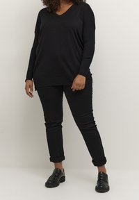 Pull en maille noire avec un col en V, associé à un pantalon noir droit et des mocassins noirs. Le pull présente une coupe décontractée et des accents côtelés.