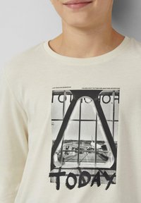 Kremowa koszulka z długim rękawem z czarno-białym nadrukiem przedstawiającym scenę na lotnisku oraz napisem "TODAY" u dołu.