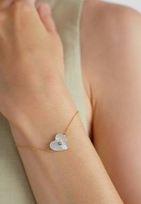 Bracciale in oro con charm a forma di cuore caratterizzato da una superficie testurizzata e un dettaglio centrale a forma di stella. Il charm è bianco e riflettente.