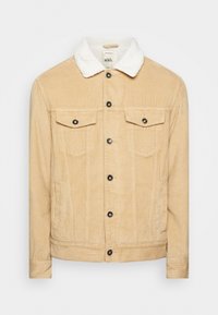 Beige manchesterjacka med vit fuskpälskrage, med två bröstfickor, svarta knappar och ribbade mudd och fåll.