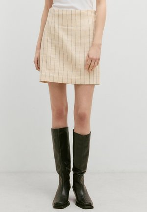 Een beige minirok met verticale blauwe strepen, gemaakt van textuurstof. Gecombineerd met kniehoge zwarte leren laarzen met een vierkante neus.