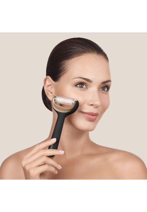 Femme aux cheveux lisses utilise un rouleau facial texturé à poignée noire sur sa joue sur un fond neutre.