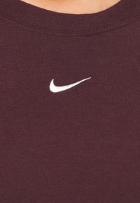 Bordo medvilninis marškinėliai su rauktu apykakle ir mažuoju baltu siuvinėtu "Nike" logotipu krūtinėje. Lygi tekstūra.