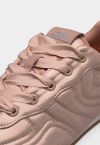 Baskets en satin rose clair avec de larges lacets en satin, œillets beige et une étiquette de languette à logo, vue en gros plan.