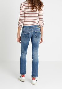 Slim-fit modré džíny s mírně vybledlým vzhledem, designem pěti kapes a švovými detaily. V kombinaci s bílými teniskami s červenými akcenty.