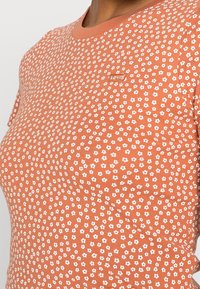 Krátký rukáv broskvové tričko s bílým květinovým potiskem, žebrovanou strukturou a malým vyšitým logem Levi's na hrudi.