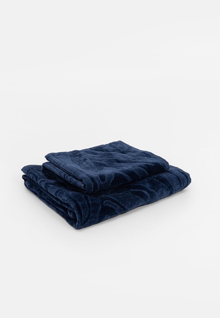 Dos toallas oscuras plegadas de color azul con un sutil patrón texturizado apiladas sobre una superficie blanca.