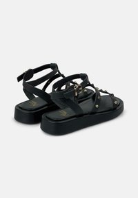 Sandali platform neri con cinturini regolabili, borchie dorate e suola liscia. Chiusura con fibbia per una vestibilità sicura.