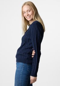 Navy blauwe gebreide trui met een gestructureerd kabelpatroon, ronde halslijn en ribgebreide manchetten en onderkant, gecombineerd met blauwe jeans.