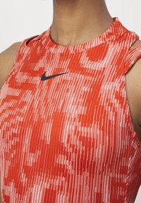 Gros plan d'une personne portant un haut de sport Nike sans manches à motifs rouge et rose avec un logo Nike swoosh noir sur la poitrine.