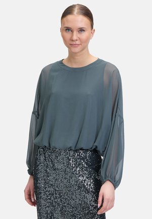 Langærmet, teal bluse i et let materiale med en afslappet pasform, parret med en funklende sort pailletnederdel. Den glatte tekstur står i kontrast til pailletterne.