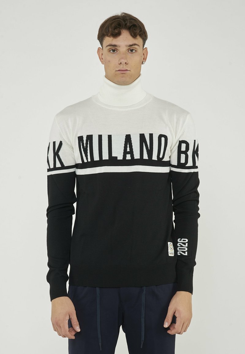 Maglione a collo alto bianco e nero con stampa del testo "MILANO", polsini e orlo a costine, e un'etichetta con "2026" sulla manica.