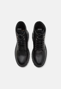 Bottines en cuir noir avec lacets, texture lisse, forme de bout arrondi et œillets en argent. Détails de couture subtils autour de la semelle.