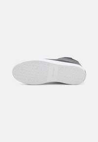 Semelle de chaussure droite avec motif texturé du logo Calvin Klein sur une semelle extérieure en caoutchouc blanc sur un fond blanc uni.
