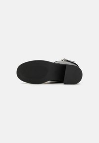 Black heeled sandal with a smooth leather upper and a rubber sole. Features a buckle accent and a textured grip on the sole for stability.