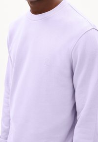 Ljuslila sweatshirt med rund halsringning, mjuk textur och broderad logotypdetalj på bröstet. Har långa ärmar och en avslappnad passform.