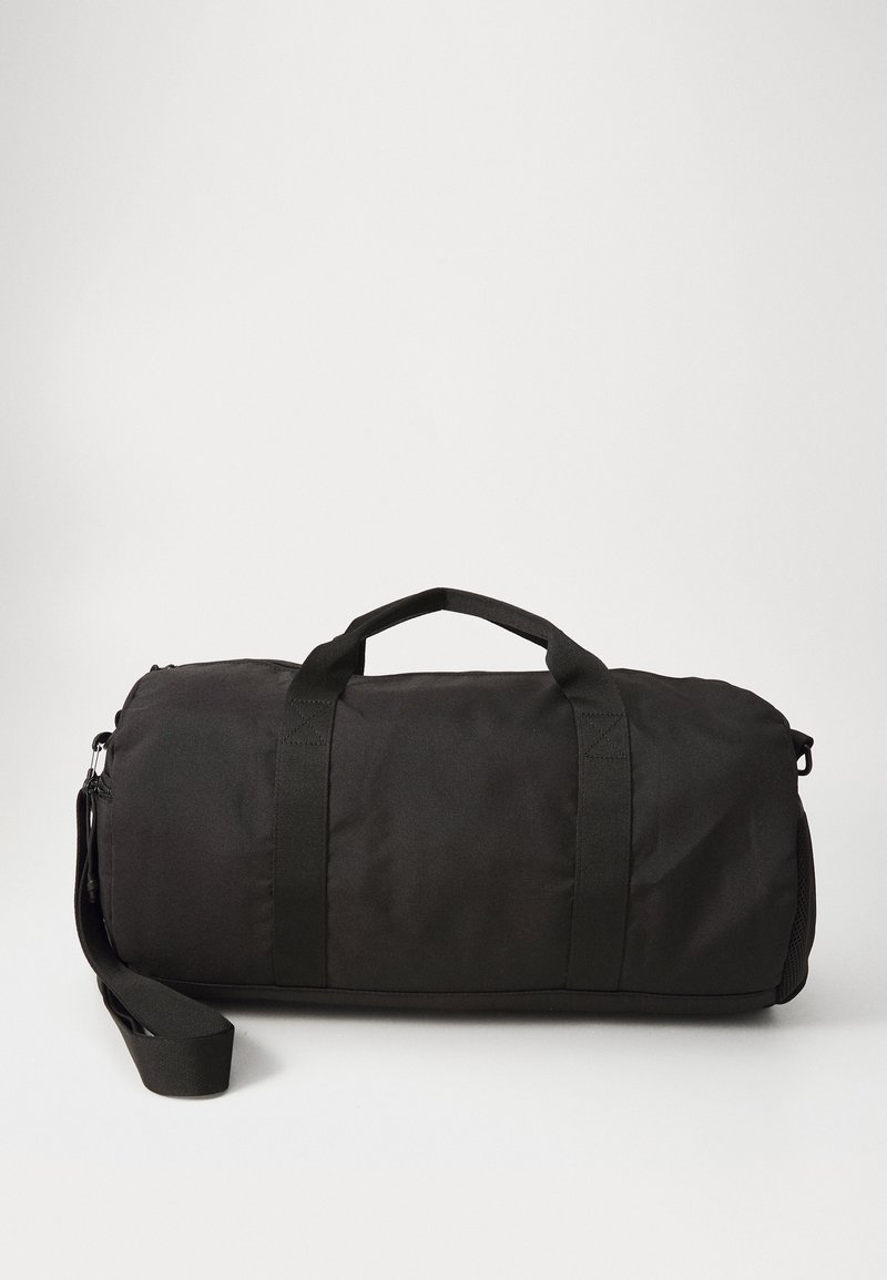 Sac de sport noir en tissu durable, doté de deux poignées supérieures, d'une bandoulière amovible et d'une forme lisse et arrondie.