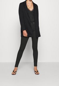 Czarny dopasowany żakiet na paski z body oraz ciemnymi wąskimi dżinsami. Czarne sandały na paski uzupełniają stylizację. Gładkie tekstury, dopasowany krój.