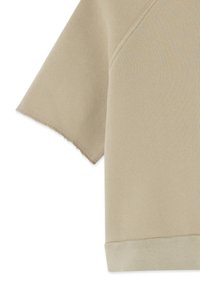 Chemise beige à manches courtes en tissu doux, avec un bord légèrement effiloché sur les manches et un ourlet côtelé en bas.