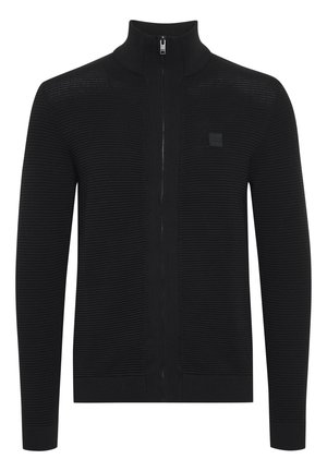 Juodas zip-up megztinis su reljefiniu tekstūru, aukštu apykaklė, ir mažas logotipo ženklas ant krūtinės. Užbaigia ilgos rankovės ir prigludusi konstrukcija.