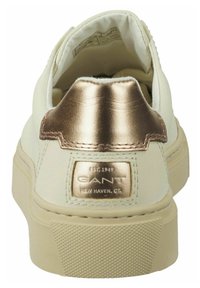 Weißer Sneaker mit metallisch goldenem Fersenlasche, strukturierter Gummisohle und Logodetail auf der Rückseite. Glattes synthetisches Material durchgehend.