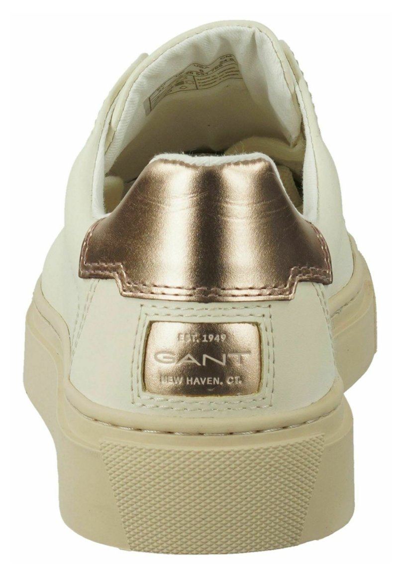 Vit sneakers med en metallisk roséguld hälla. Har en texturerad gummisula och en varumärkesetikett på baksidan. Slät läderövre.