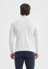 Pull en maille blanche à manches longues, avec des poignets et un ourlet côtelés. Matériau léger, design ajusté et texture lisse, montrant une simple vue arrière.