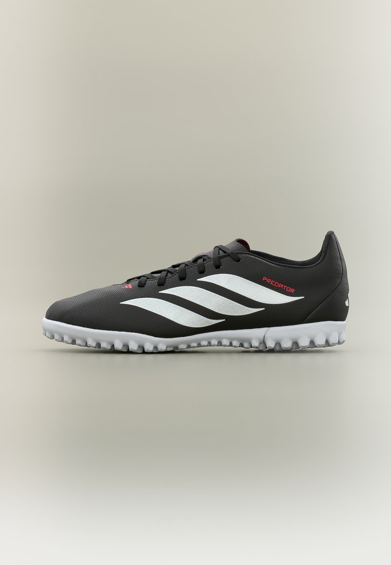 Μαύρο ποδοσφαιρικό παπούτσι Adidas Predator με λευκό λογότυπο τριών ραβδώσεων, μικρό κόκκινο κείμενο "Predator" και λευκή υφασμάτινη σόλα κατάλληλη για τεχνητό χλοοτάπητα.