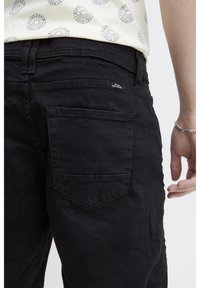 Sorte denim jeans med en baglomme med en buet søm og et lille mærke. Stoffet har en synlig tekstur med en mat finish.