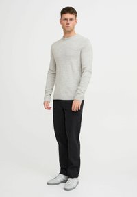 Maglione grigio chiaro a maniche lunghe con collo rotondo, abbinato a pantaloni neri e sneakers grigie. Design semplice con polsini e orlo a coste.