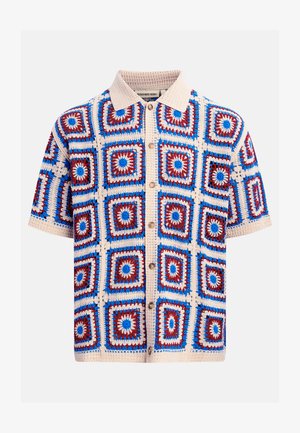 Camisa de manga corta con cuello beige y patrón de crochet con motivos cuadrados en rojo, azul y beige sobre un fondo claro.