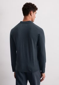 Langsleeve, donkergrijs shirt van zachte stof met een kraag, voorzien van een afgeronde zoom en raglanmouwen, gezien vanaf de achterkant.