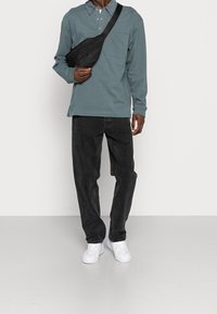 Long-sleeve teal polo shirt with a pocket, paired with black corduroy pants and white sneakers. The outfit includes a black crossbody bag.