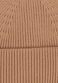 Close-up of beige knitted fabric showing vertical ribbing and interlocking knit stitches in a folded textile piece.