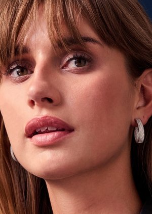 Orecchino a cerchio in argento con design curvo, caratterizzato da una superficie testurizzata e pietre preziose infilate, mostrato sull'orecchio di un modello.
