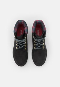 Botas negras impermeables con ojales dorados, cordones grises y un cuello acolchado con patrón de cuadros en rojo y azul. Acabado de ante suave.